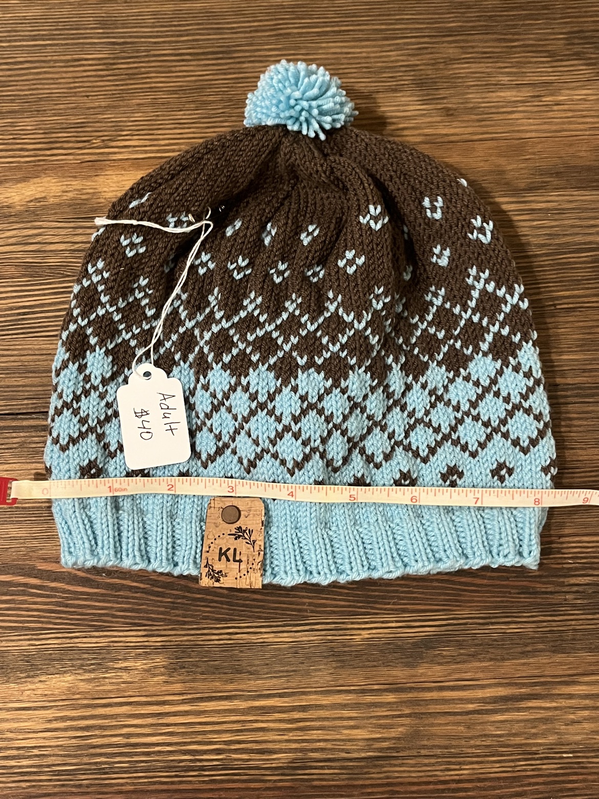 Adult hand knit wool hat shown with a measuring tape across the brim