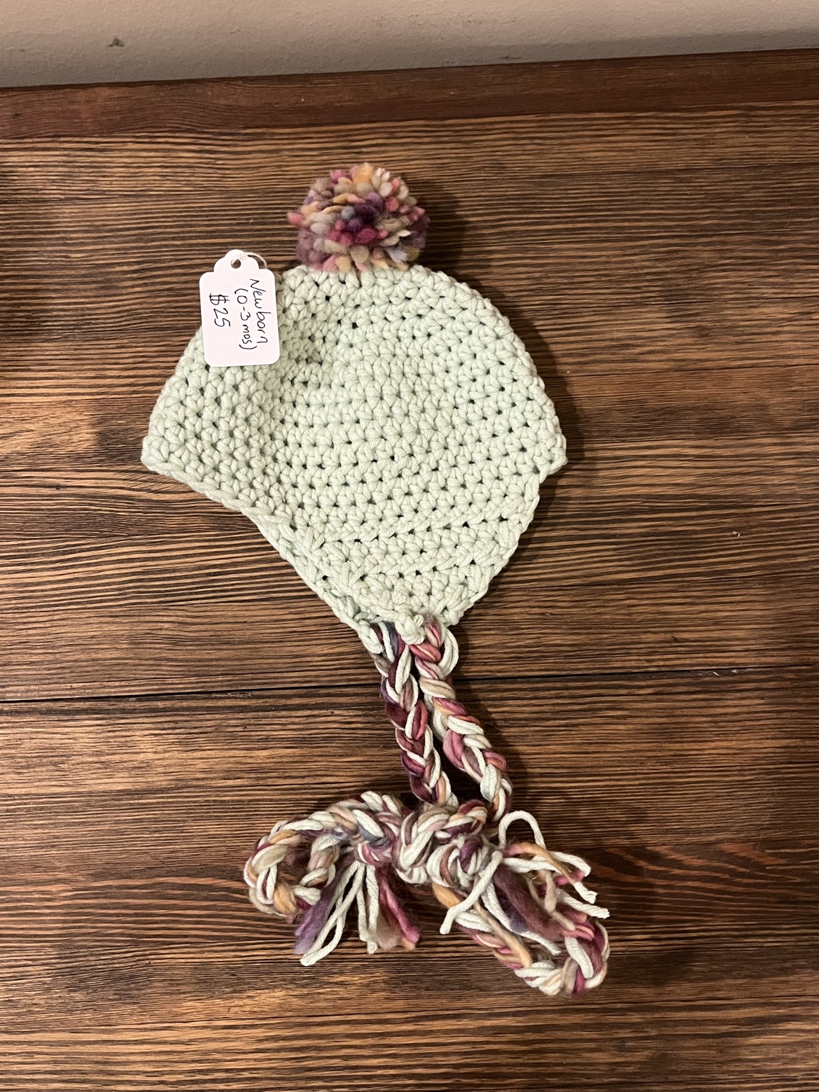Mint green hand crochet baby ear flap hat with a multicolor pom-pom and braided ties