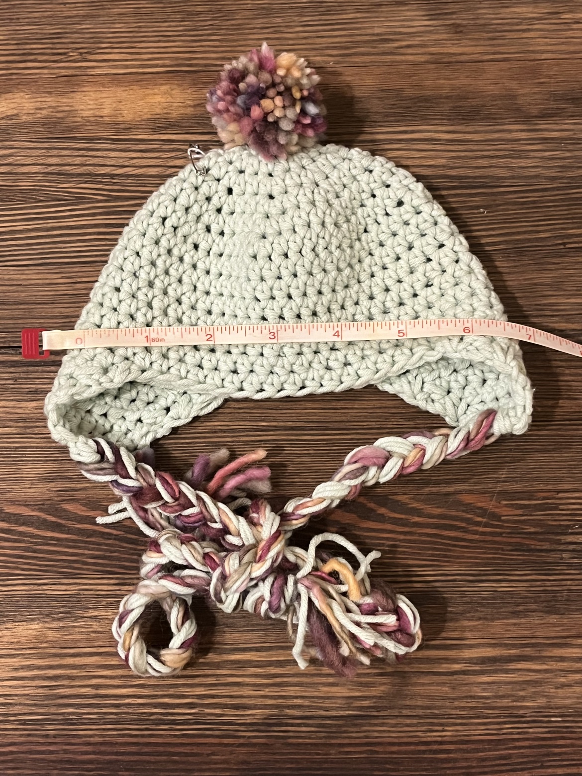Baby ear flap hat shown with a measuring tape across its width