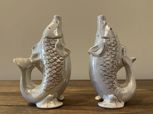 Two white porcelain fish-shaped vases with gold scales and red fins on a wooden surface
