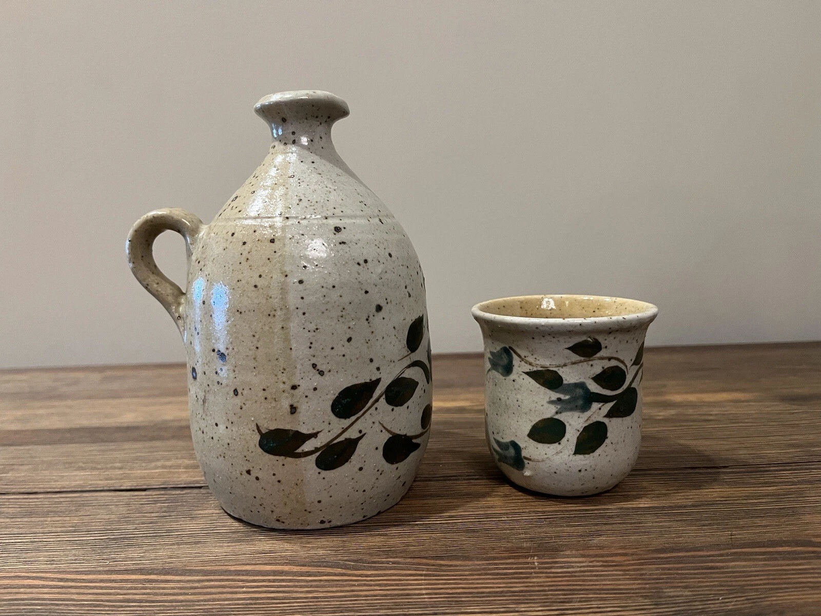 Hand-painted stoneware pitcher and cup with a green floral and leaf pattern