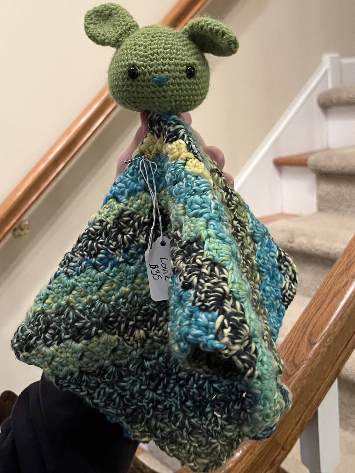 Crochet bunny lovie with a green bunny head and a textured teal, yellow, black, and cream blanket