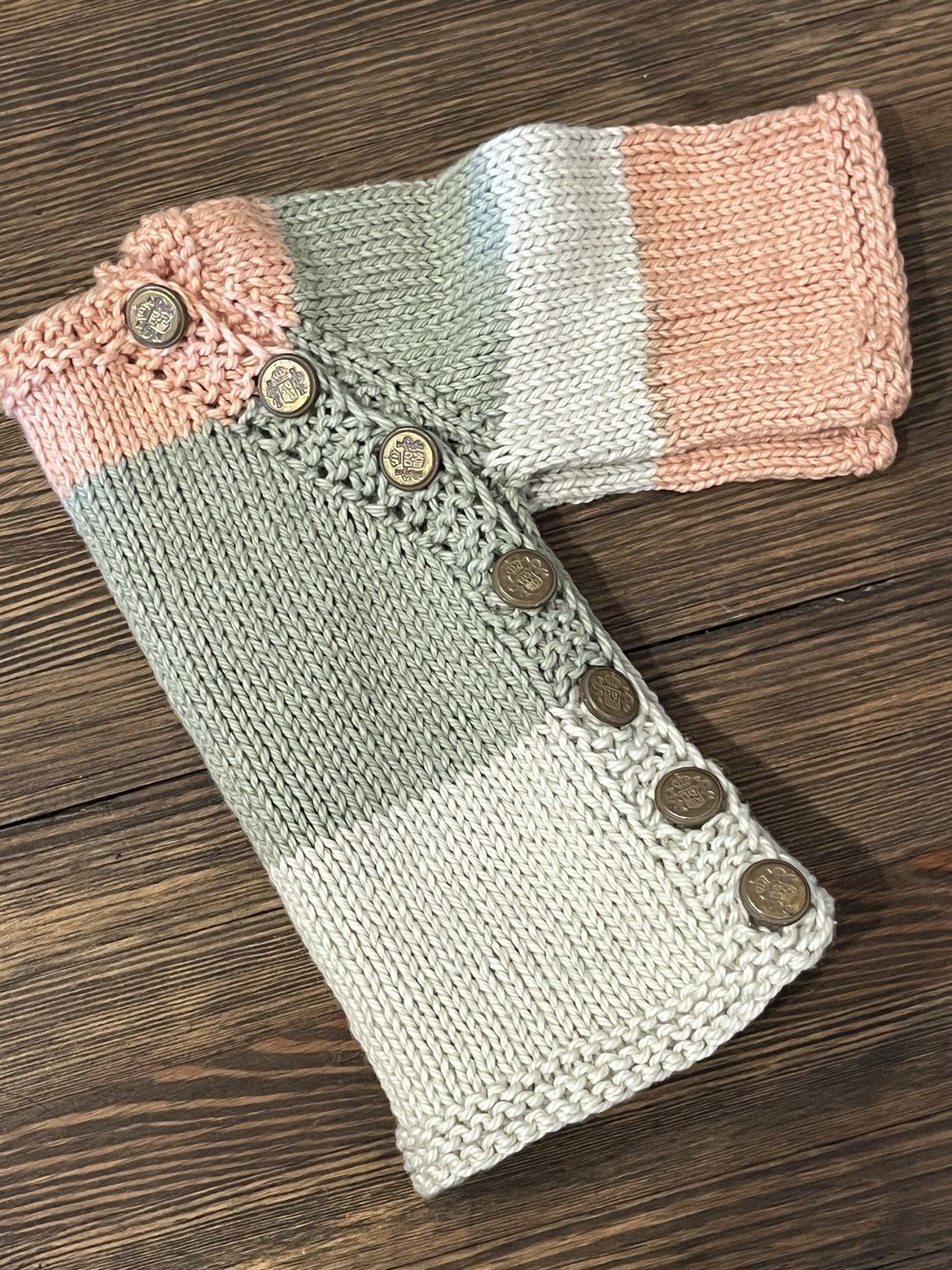 Folded hand-knit baby sweater showing its peach, sage, and cream color blocks