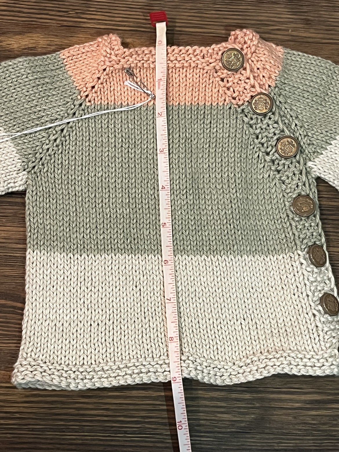 Baby sweater with a measuring tape showing an approximate length of 9 inches