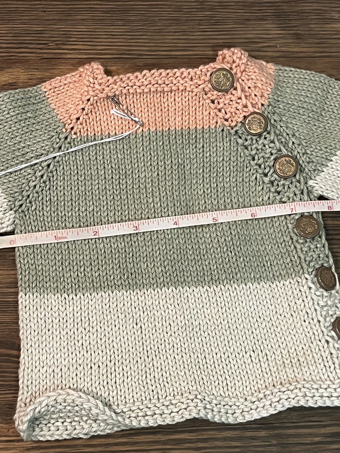 Baby sweater with a measuring tape showing an approximate width of 7.5 inches
