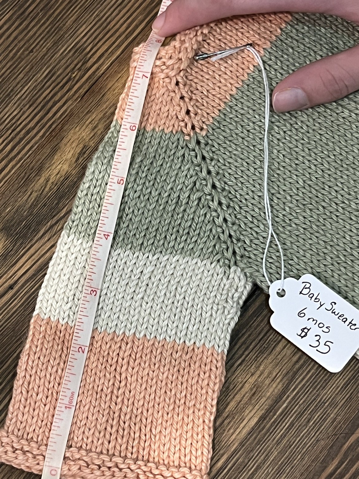Baby sweater sleeve with a measuring tape showing an approximate length of 8 inches