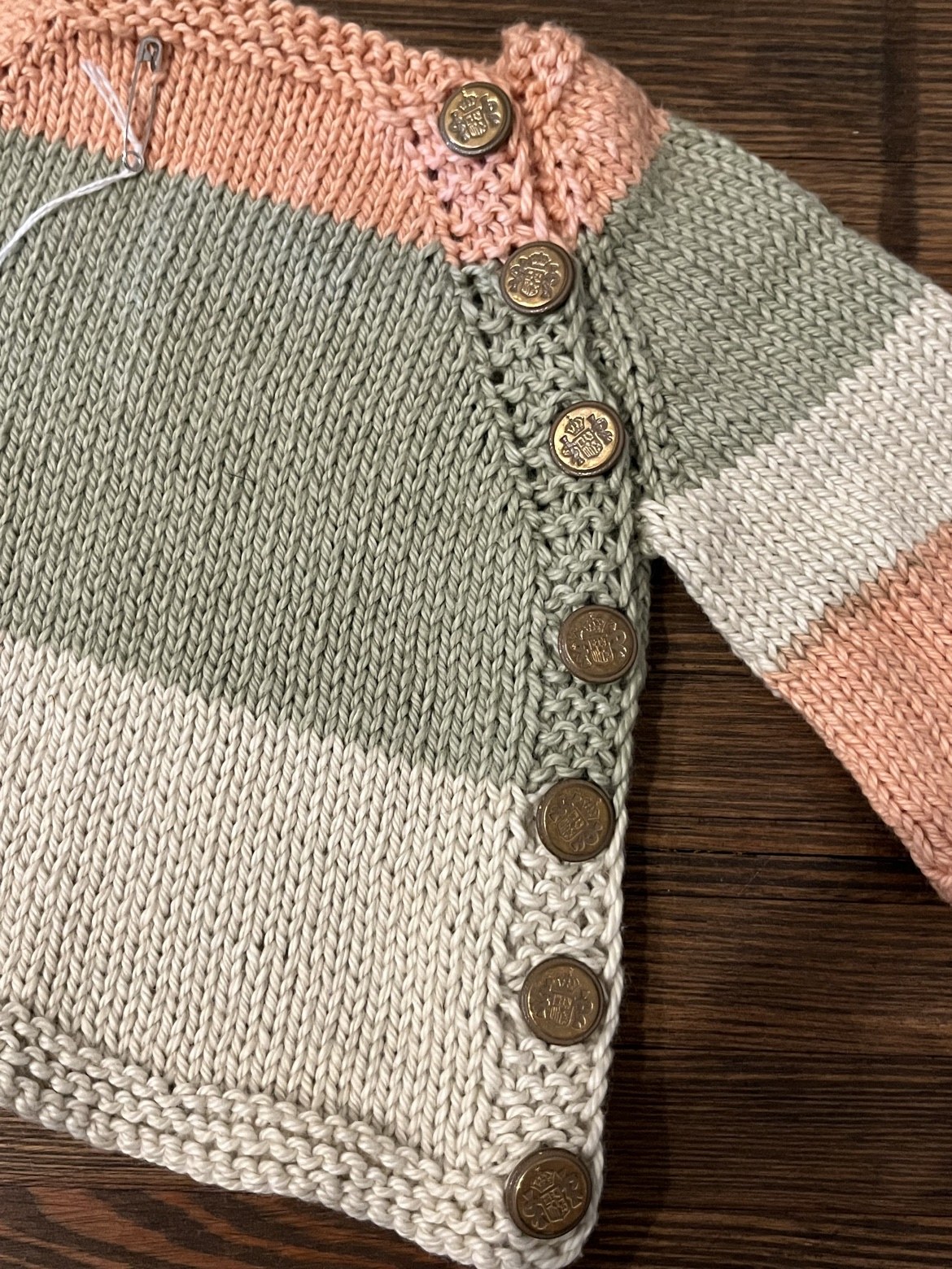 Close-up of the baby sweater’s knit texture and bronze-tone side buttons