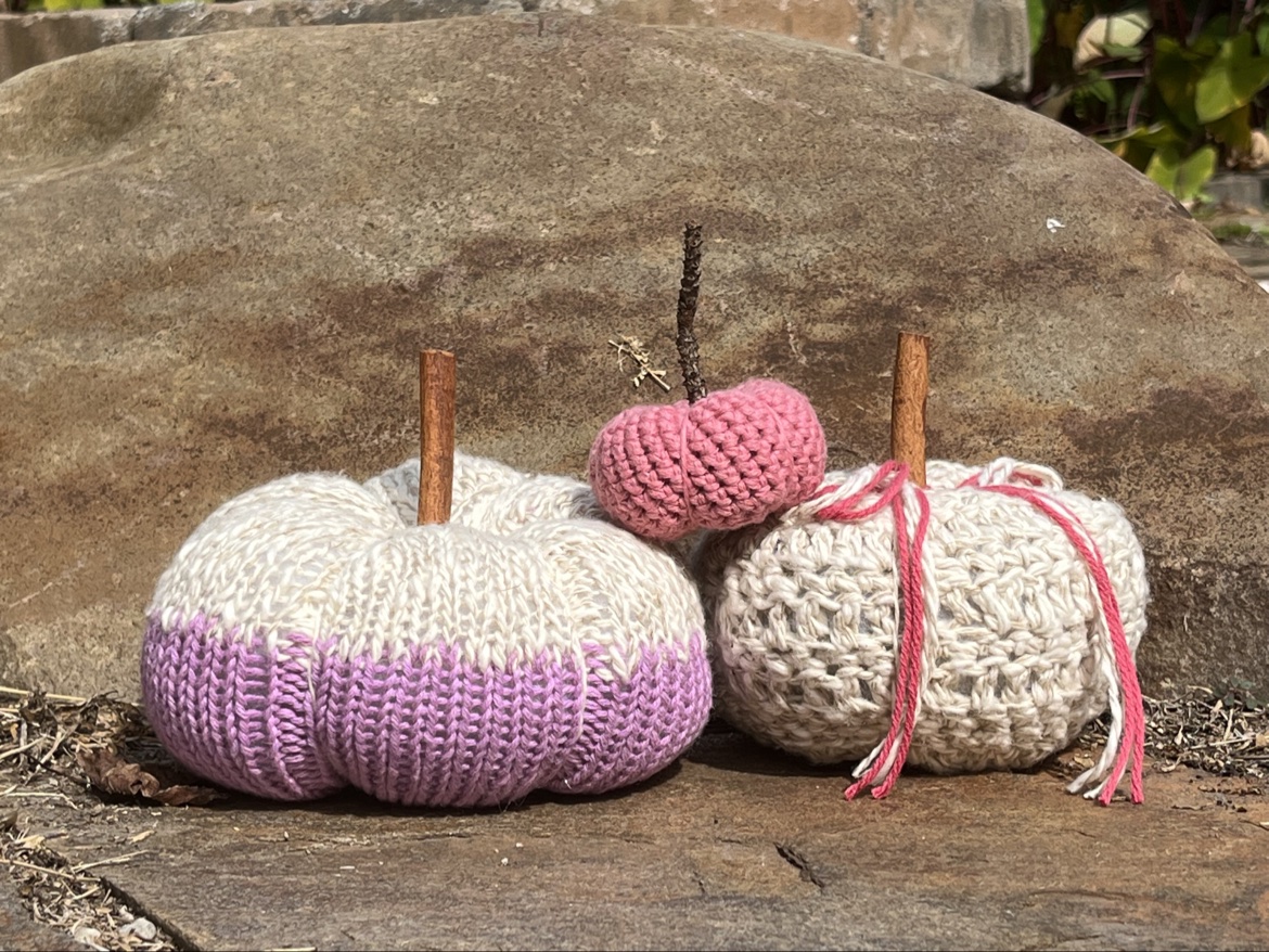 Purple, cream, and pink hand knit and crochet pumpkins arranged outdoors