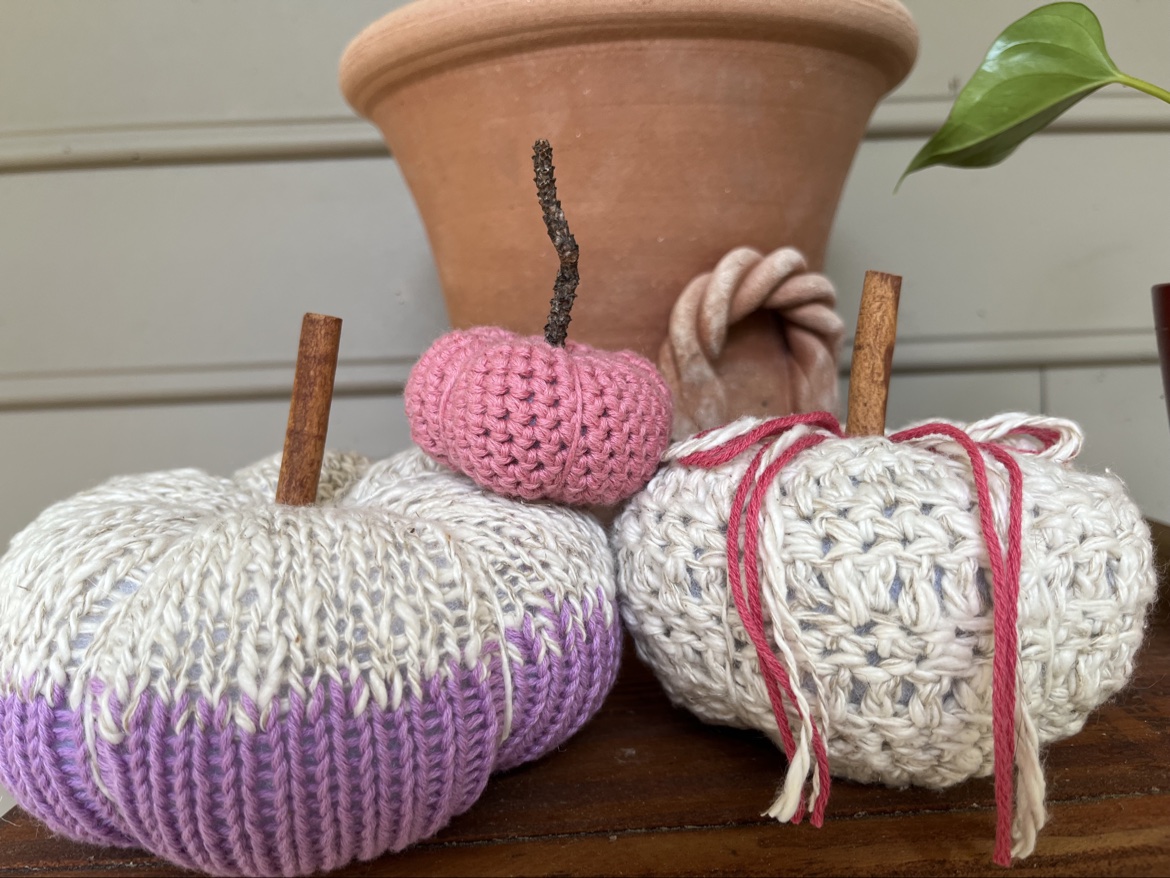 Purple, cream, and pink hand knit and crochet pumpkins displayed beside a terracotta pot