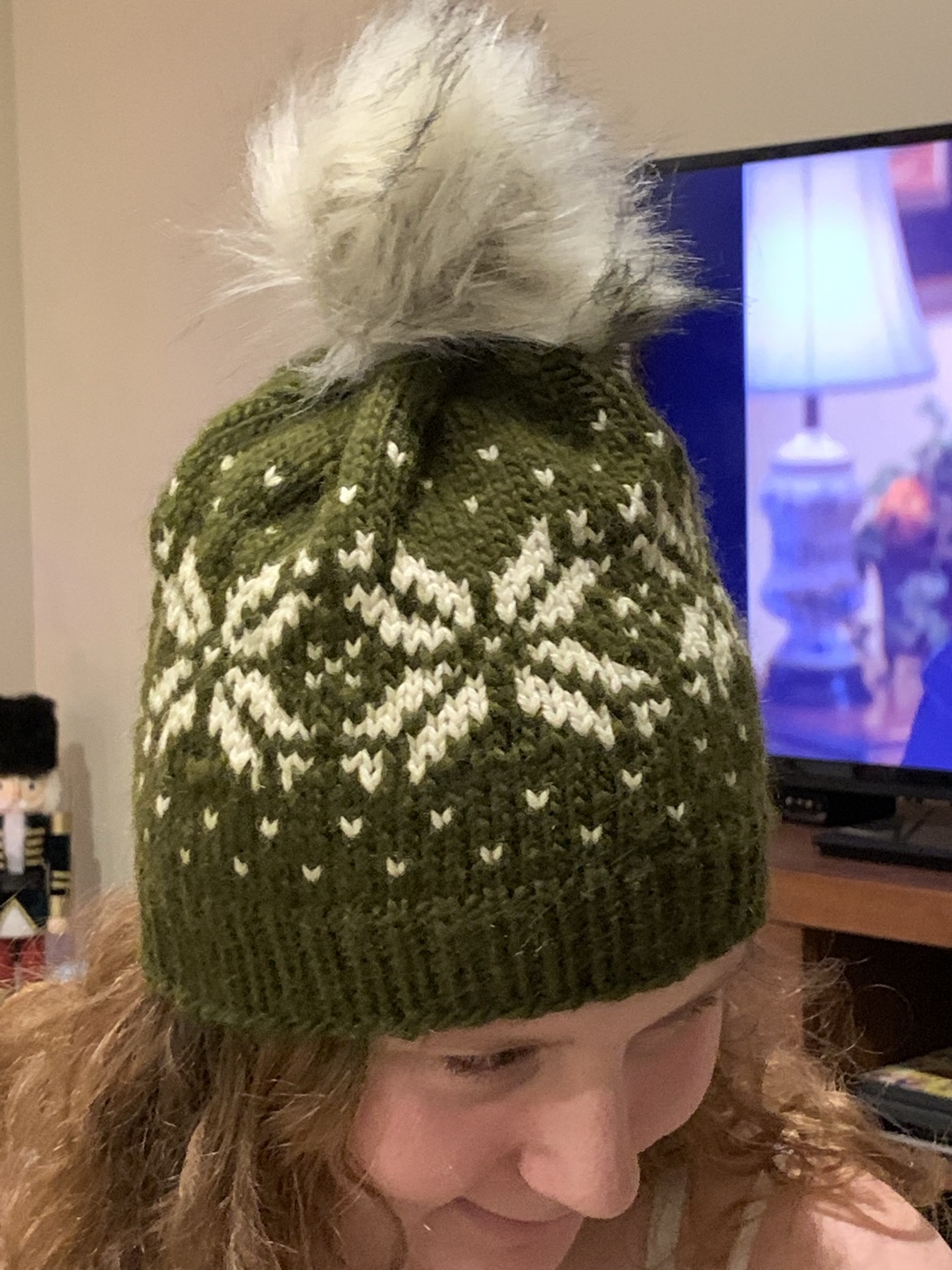 Olive green and cream snowflake knit hat with a faux-fur pom-pom