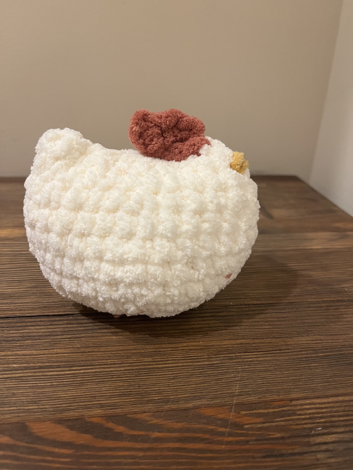 Side view of a crochet white chicken with a rust comb and mustard beak