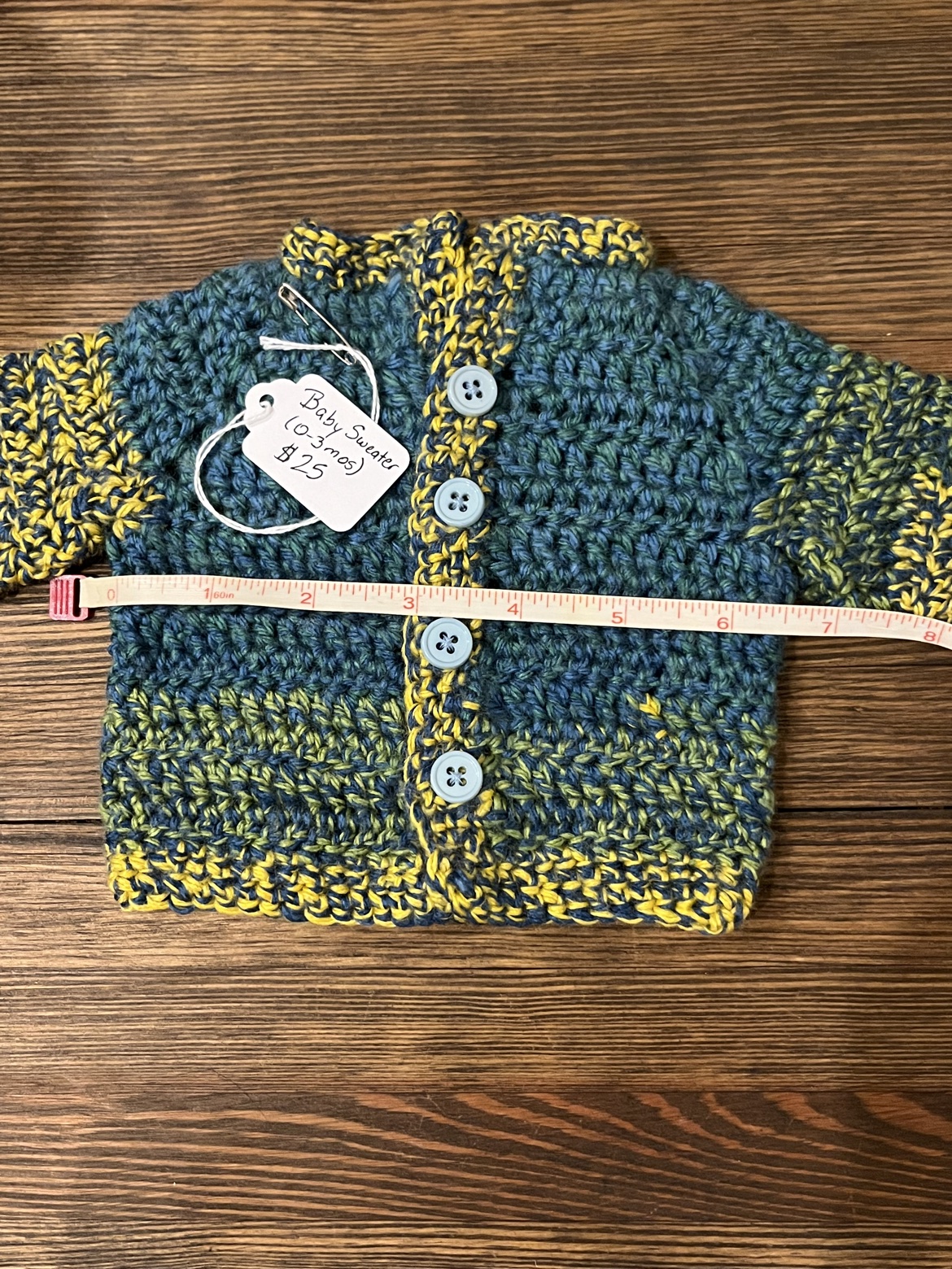 Crochet baby sweater shown with a measuring tape across its width