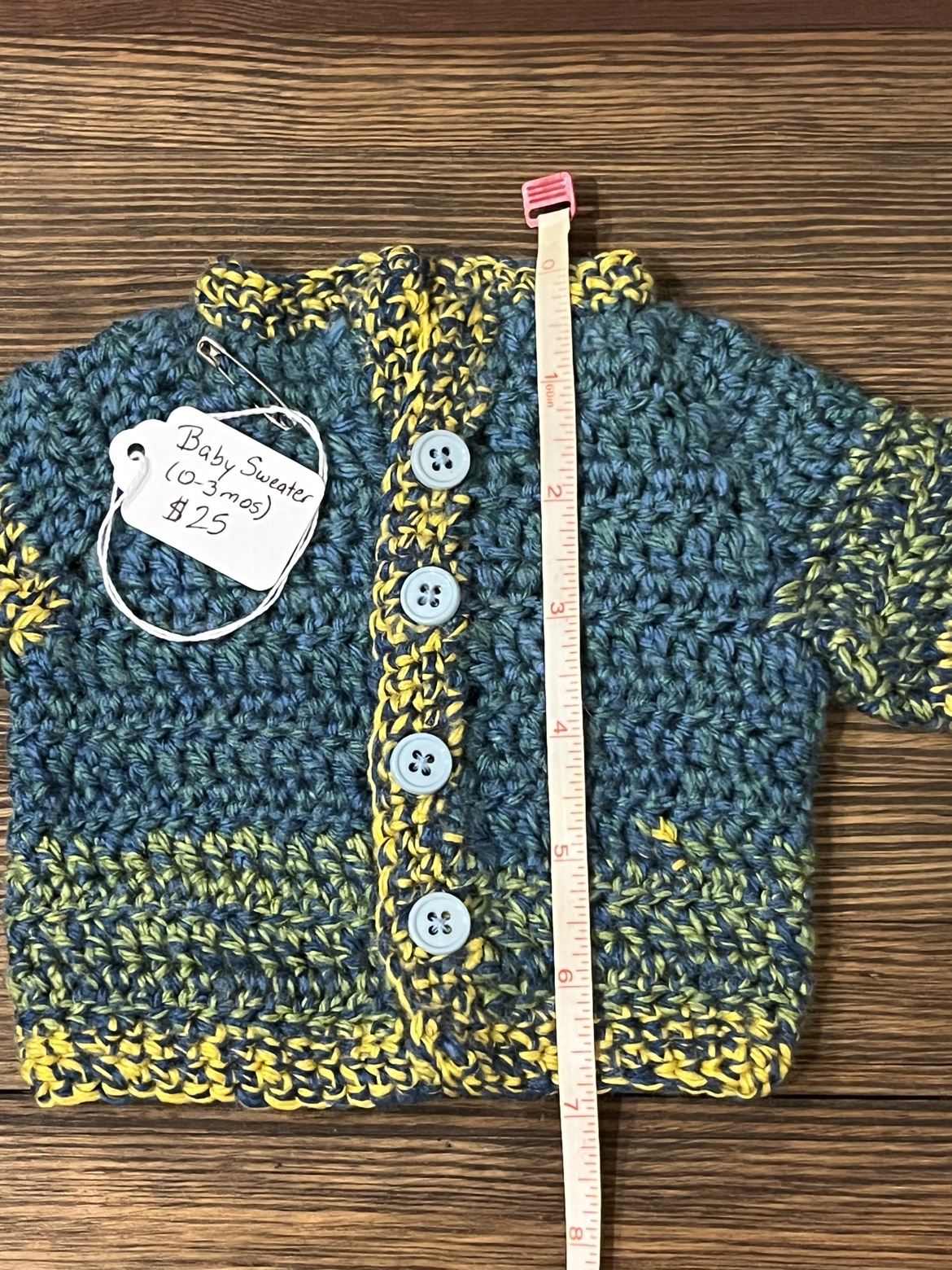 Crochet baby sweater shown with a measuring tape from shoulder to hem