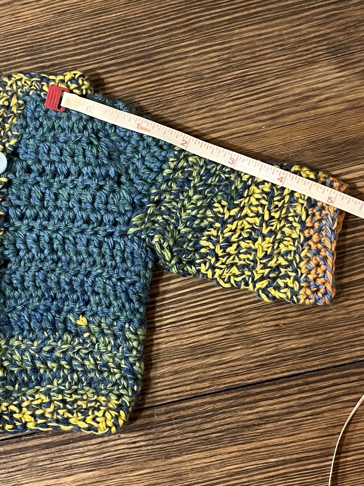 Crochet baby sweater shown with a measuring tape along the sleeve