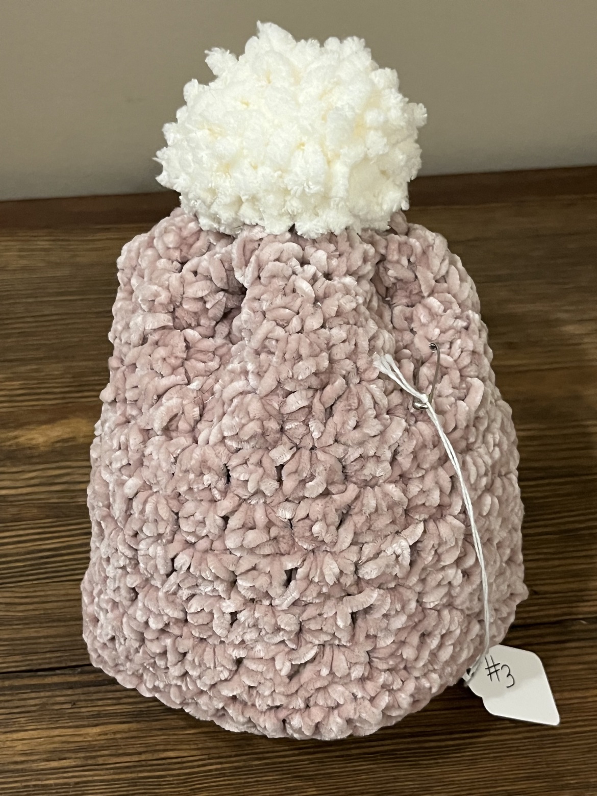 Pink crochet toddler hat displayed upright with its white Pom Pom