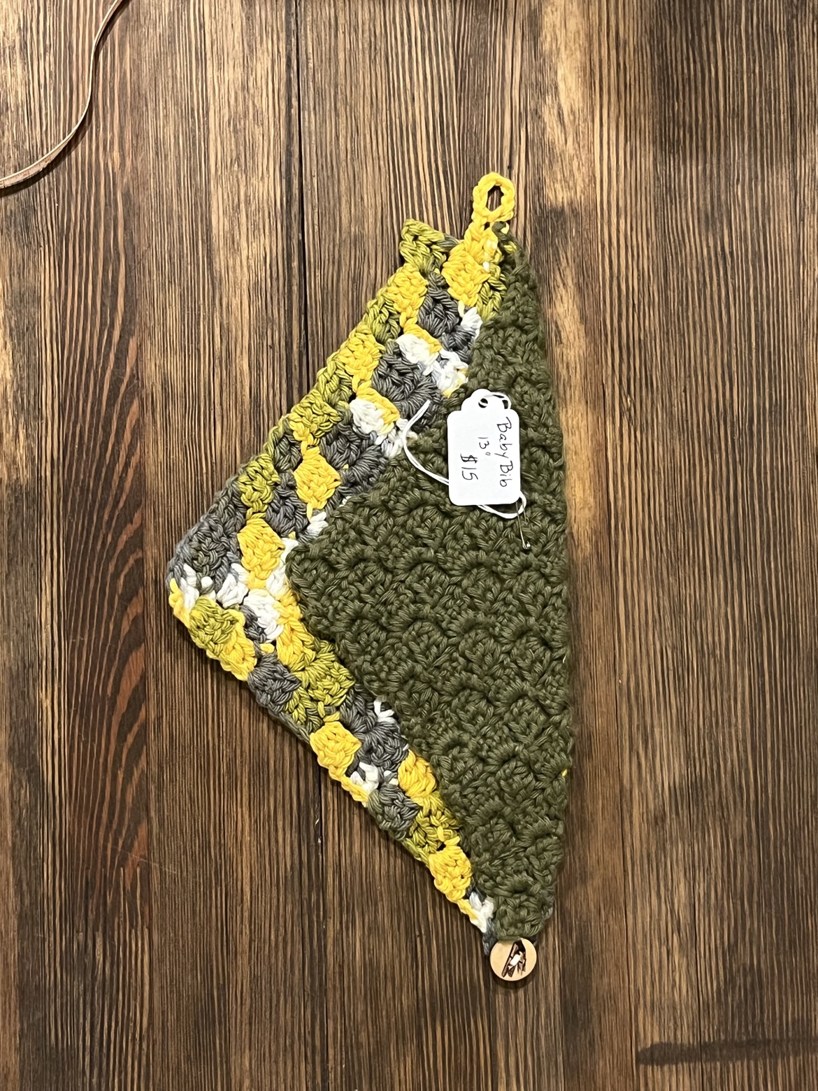 Dark green and multicolor crochet baby bib scarf laid flat to show its triangular shape