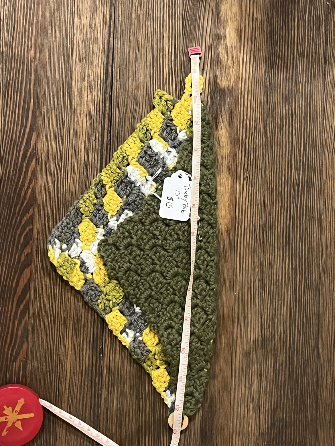 Dark green and multicolor crochet baby bib scarf shown with a measuring tape